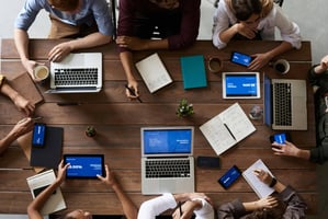 A bird's eye view of a group of people around the table with their laptops 